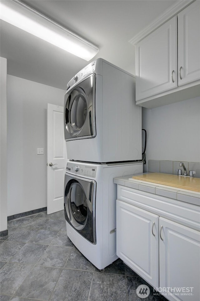 laundry room with baseboards, stacked washing maching and dryer, and cabinet space