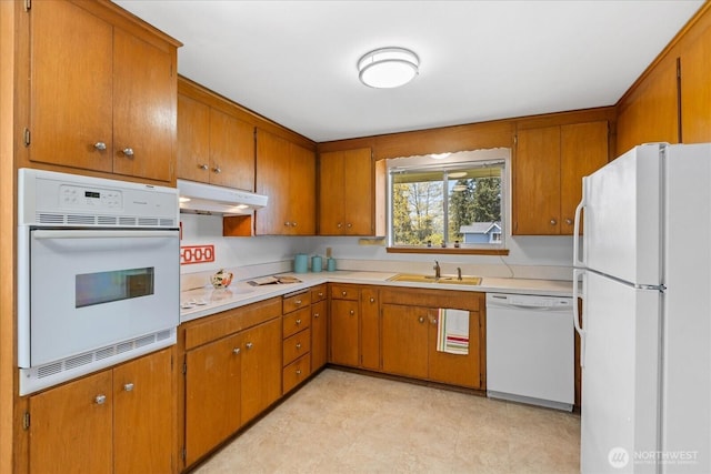 kitchen featuring white appliances, light countertops, under cabinet range hood, brown cabinets, and a sink