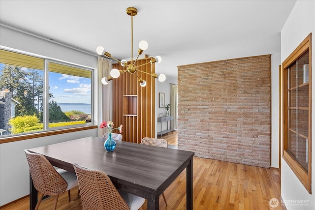 dining room with an inviting chandelier, light wood-type flooring, and brick wall