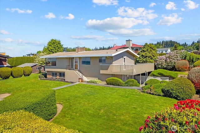 rear view of property featuring a chimney, a yard, and a balcony