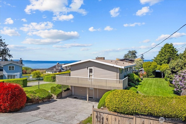 exterior space with an attached garage, a water view, concrete driveway, a balcony, and a lawn
