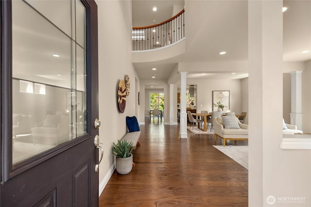 foyer entrance featuring a high ceiling, dark wood finished floors, recessed lighting, baseboards, and decorative columns
