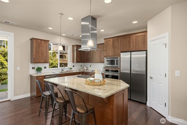 kitchen with light stone countertops, a sink, stainless steel appliances, decorative backsplash, and island range hood