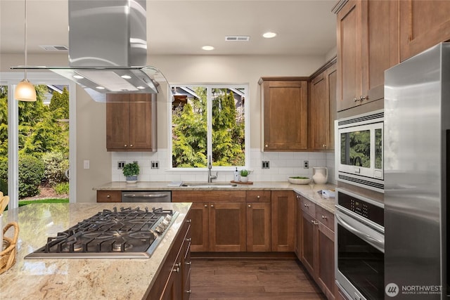 kitchen featuring a sink, stainless steel appliances, island exhaust hood, dark wood-type flooring, and backsplash