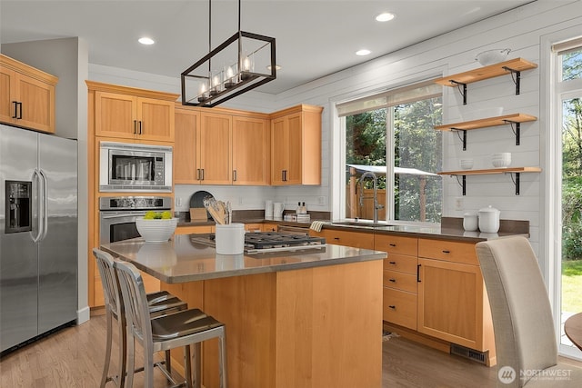 kitchen featuring stainless steel appliances, dark countertops, a sink, and light wood-style flooring