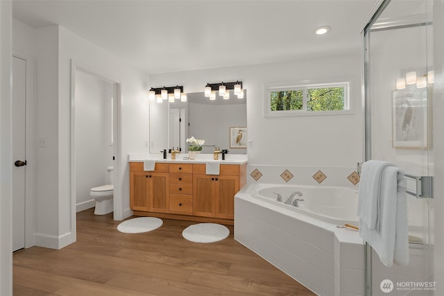 full bath with double vanity, toilet, wood finished floors, a garden tub, and a stall shower