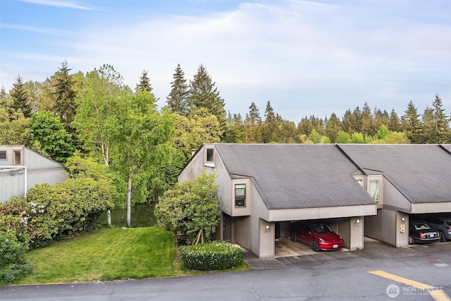 view of front of home featuring covered parking, a shingled roof, and a front yard