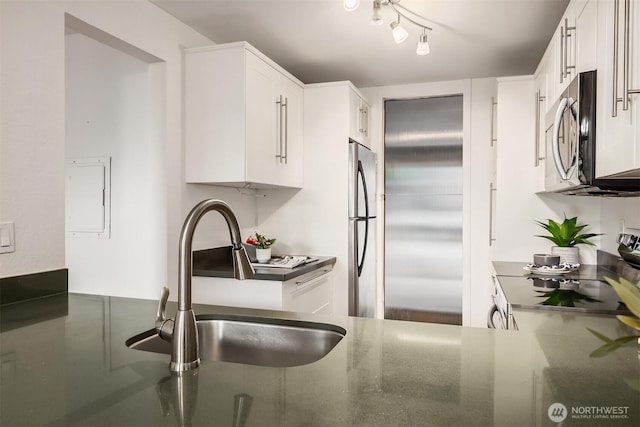 kitchen with stainless steel appliances, white cabinets, a sink, and dark stone countertops