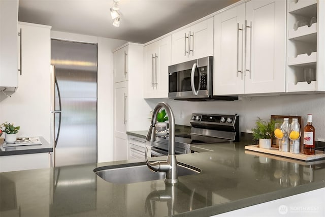 kitchen featuring stainless steel appliances, a sink, white cabinets, and dark stone counters
