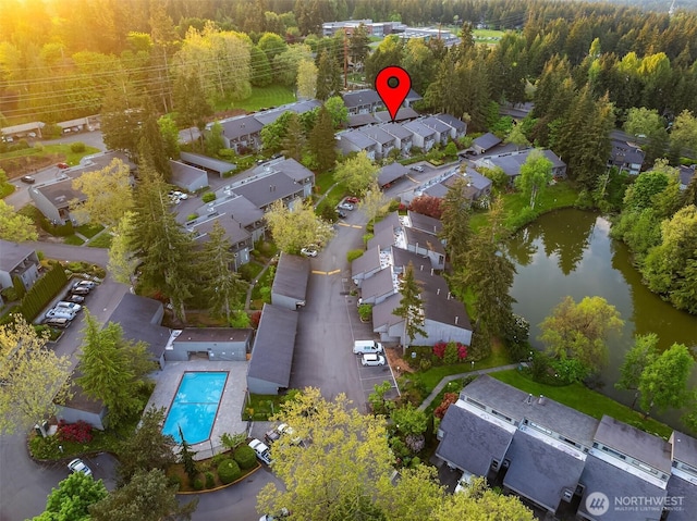 aerial overview of property's location featuring a pool, nearby suburban area, a forest, and a nearby body of water