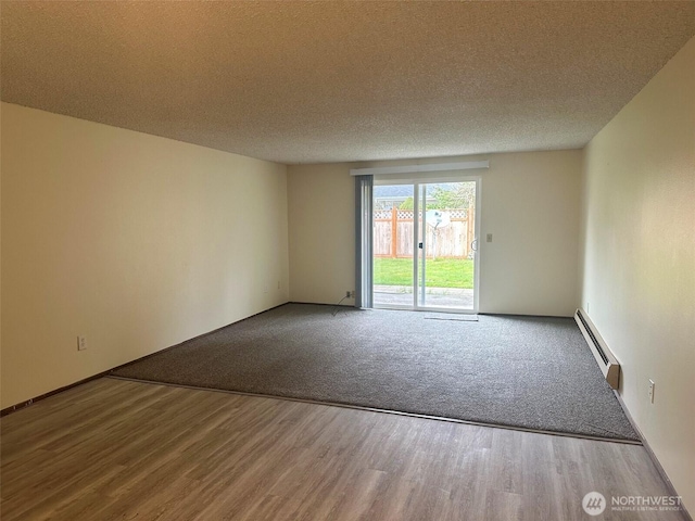 spare room featuring a baseboard radiator, wood finished floors, baseboards, and a textured ceiling