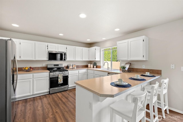 kitchen featuring white cabinets, light countertops, stainless steel appliances, a peninsula, and dark wood-type flooring