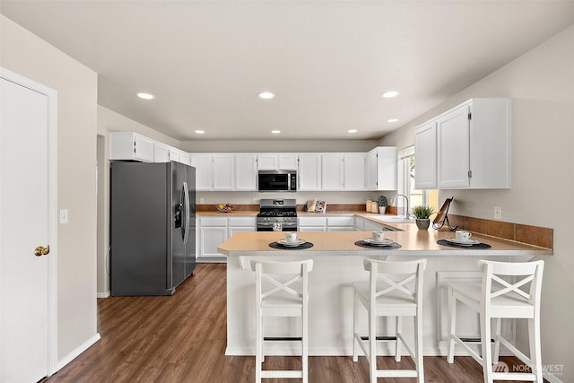 kitchen with appliances with stainless steel finishes, a sink, light countertops, a peninsula, and dark wood-type flooring