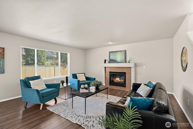 living area with a tiled fireplace, baseboards, and wood finished floors