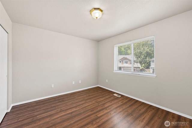 empty room with baseboards, visible vents, and wood finished floors