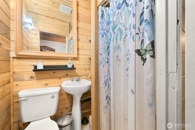 full bath with wooden walls, toilet, and a sink