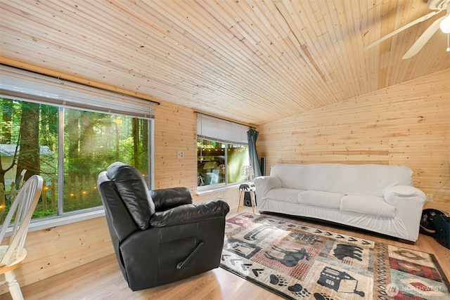 living area featuring ceiling fan, wood finished floors, wooden walls, and vaulted ceiling