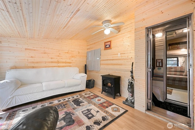 living room featuring wooden walls, ceiling fan, a wood stove, wood finished floors, and wood ceiling