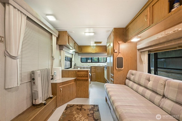 kitchen with brown cabinetry, light countertops, a peninsula, radiator heating unit, and black oven