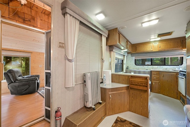kitchen featuring brown cabinetry, light countertops, wood walls, and oven