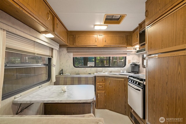 kitchen with white gas range, brown cabinetry, range hood, fridge, and light countertops