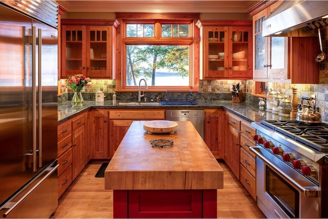 kitchen with tasteful backsplash, wood counters, a sink, premium appliances, and wall chimney exhaust hood
