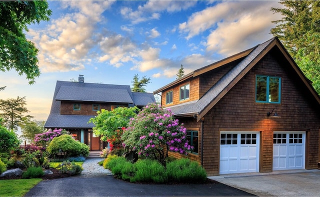 view of front of property featuring driveway, a chimney, a shingled roof, and an attached garage