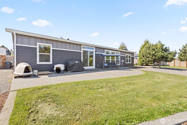 rear view of house with board and batten siding, a lawn, and a patio area