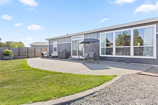 rear view of property featuring fence, board and batten siding, a lawn, and a patio area