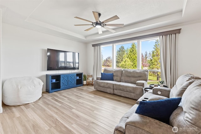 living room with light wood-style floors, ceiling fan, and a tray ceiling