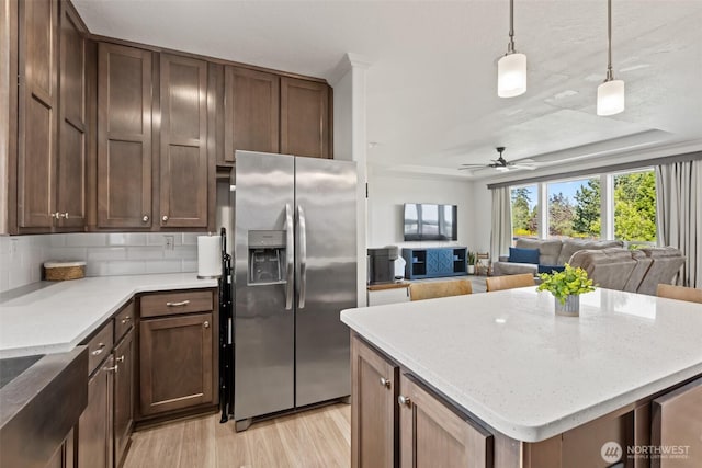 kitchen featuring light wood-style floors, stainless steel fridge, tasteful backsplash, a ceiling fan, and hanging light fixtures
