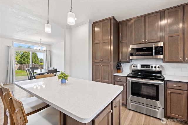 kitchen with a kitchen island, a chandelier, light wood finished floors, hanging light fixtures, and stainless steel appliances