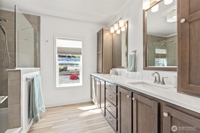 bathroom with double vanity, a tile shower, a sink, and wood finished floors