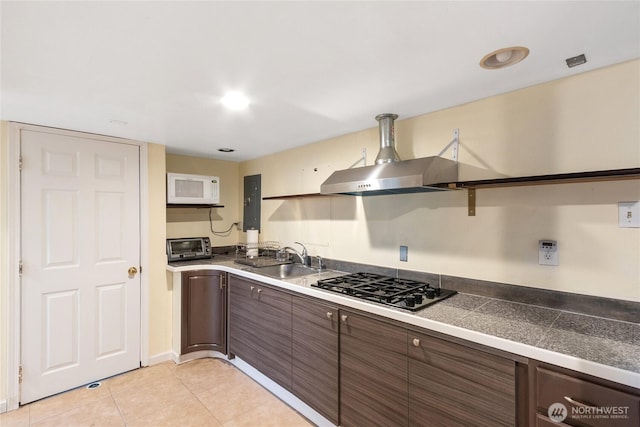 kitchen featuring white microwave, wall chimney range hood, tile counters, gas stovetop, and a sink