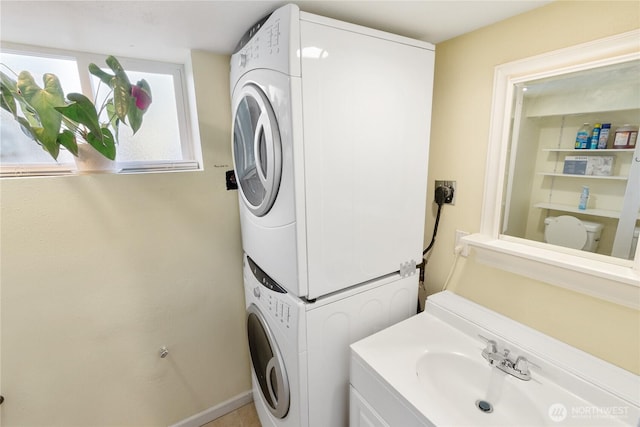 washroom with laundry area, a sink, baseboards, and stacked washer / drying machine