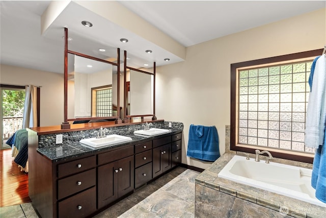 full bathroom with double vanity, a sink, a bath, and recessed lighting