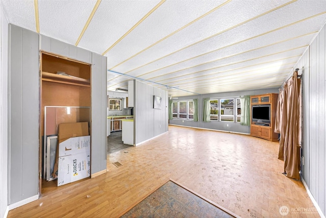 unfurnished living room featuring a textured ceiling, baseboards, and wood finished floors