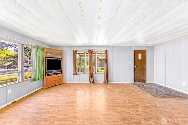 unfurnished living room with a textured ceiling, baseboards, and light wood finished floors