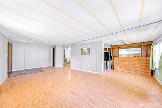 unfurnished living room featuring light wood-style floors, baseboards, and wood walls