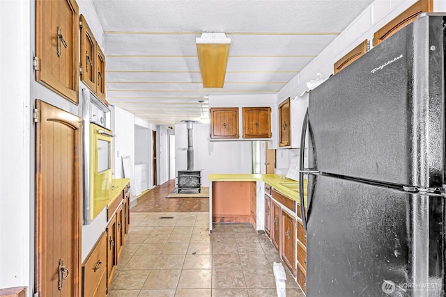 kitchen featuring a textured ceiling, a wood stove, brown cabinets, freestanding refrigerator, and a peninsula