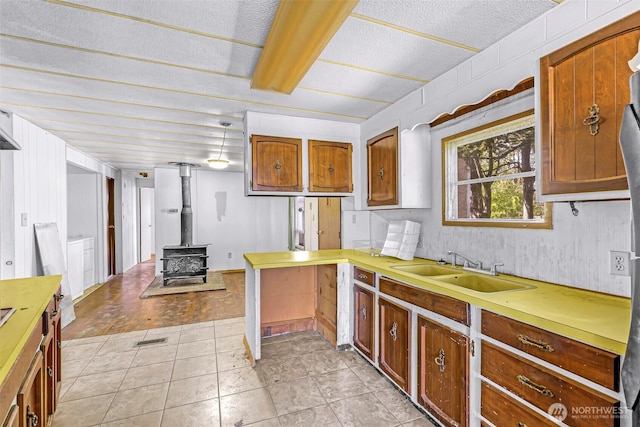 kitchen featuring a wood stove, a peninsula, light countertops, a sink, and light tile patterned floors