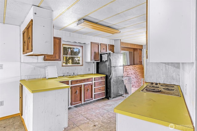 kitchen with a sink, light countertops, freestanding refrigerator, light tile patterned floors, and stainless steel electric stovetop