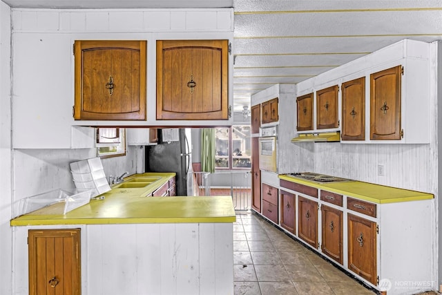 kitchen featuring electric stovetop, white oven, a sink, light countertops, and a peninsula