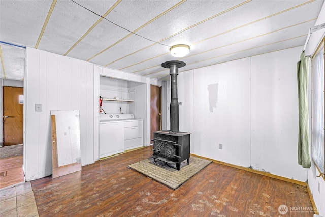 unfurnished living room with a textured ceiling, a wood stove, wood finished floors, baseboards, and washer and dryer