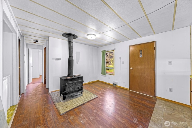 unfurnished living room featuring baseboards, a wood stove, and wood finished floors