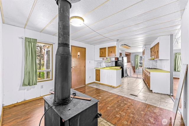 unfurnished living room featuring baseboards, a wood stove, light wood finished floors, and a textured ceiling