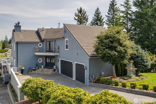 rear view of house with a chimney, an attached garage, driveway, and a balcony