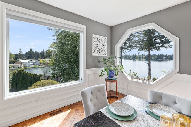 dining space with visible vents, a water view, wood finished floors, and a wainscoted wall