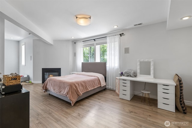bedroom featuring a glass covered fireplace, recessed lighting, light wood-style flooring, and visible vents