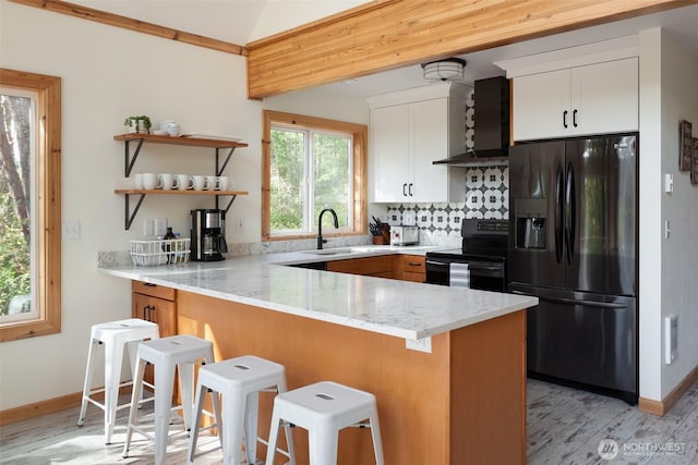 kitchen featuring light stone counters, wall chimney range hood, a sink, black appliances, and a peninsula